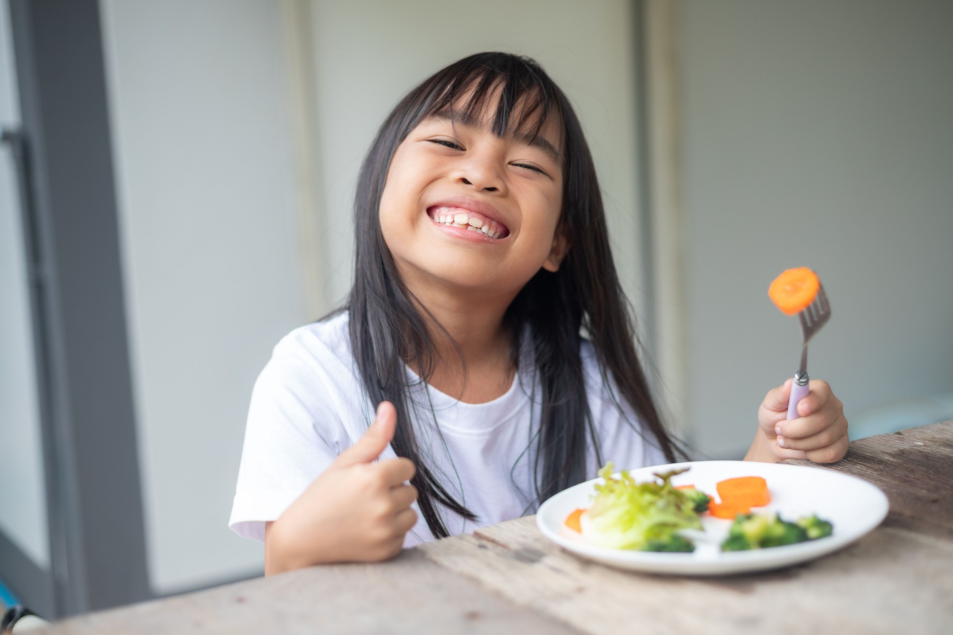 A young girl is sitting at a table with a plate of vegetables in front of her